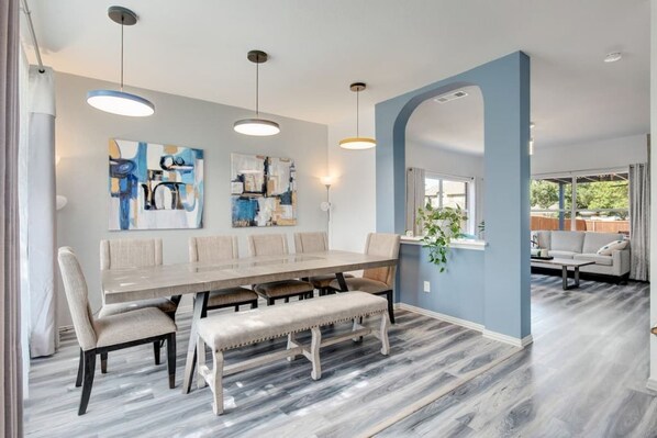 A dining area with a long table, benches, and hanging pendant lights.
