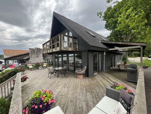 A modern house with a large deck, outdoor seating, and a stone wall. - Beautiful rental with amazing views on Donnell Lake’s North Shore, (Vandalia)