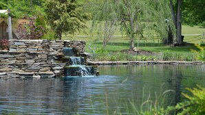 A pond with a stone waterfall, surrounded by lush greenery and trees.