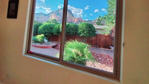 Una ventana con vistas a un patio trasero, que incluye una valla de madera, un perro blanco y una cadena montañosa.