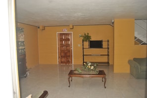 A lobby with a wooden door marked "EXIT," a wooden bench with a plant, and a grey sofa. - Superb Villa in Montego Bay (Montego Bay)