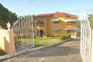 A yellow building with a red roof, a gated entrance, and a well-maintained lawn. - Superb Villa in Montego Bay (Montego Bay)