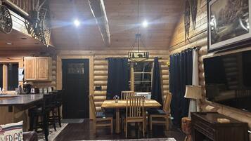 Ein Blockhaus-Interieur mit Essbereich, Küche und einem großen Flachbildfernseher.