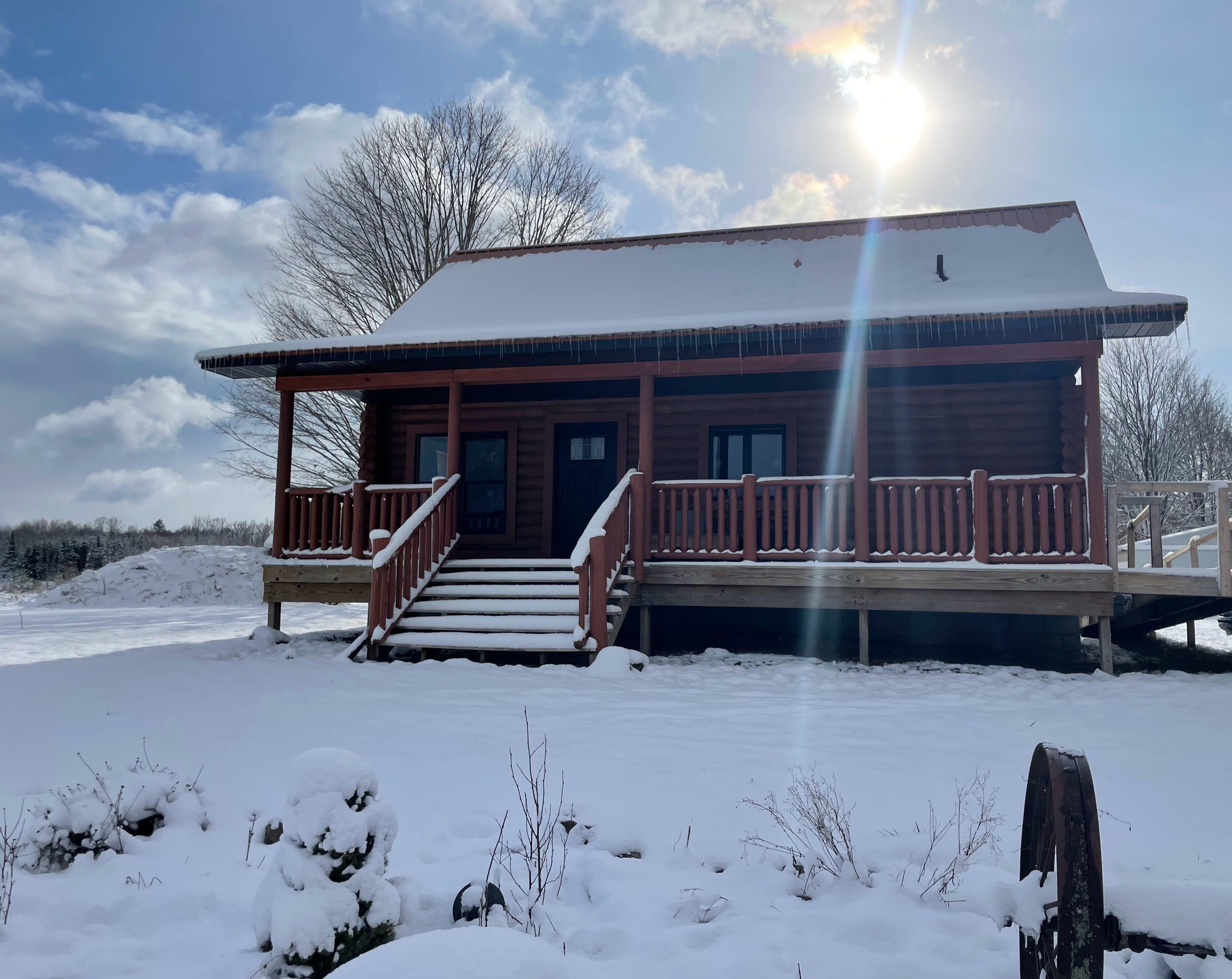 Eine Holzhütte mit Veranda, Treppe und verschneiter Landschaft.