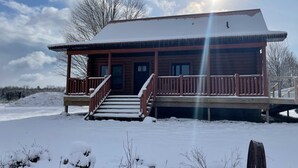 A wooden cabin with a porch, steps, and a snow-covered landscape.