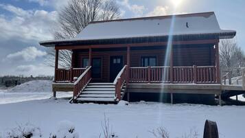 Eine Holzhütte mit Veranda, Treppe und verschneiter Landschaft.