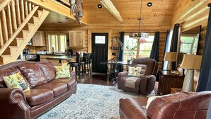 Ein gemütliches Blockhaus-Interieur mit einem Ledersofa, einem Relaxsessel, einem Essbereich und einer Küche.