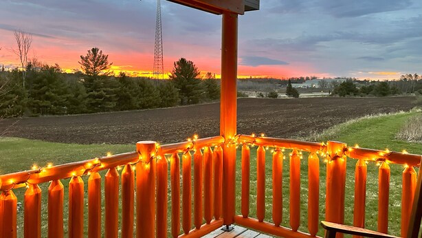 Eine Veranda mit Blick auf einen Sonnenuntergang über einem Feld, einem hohen Turm und einer Lichterkette.
