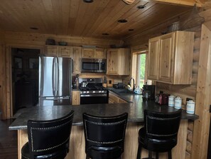 A wooden cabin kitchen with a refrigerator, stove, microwave, and bar stools.