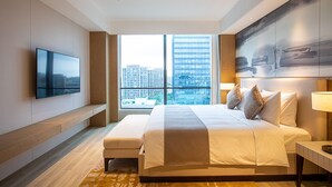 Una habitación de hotel moderna con una cama grande, un televisor de pantalla plana, vistas a la ciudad y un diseño minimalista.