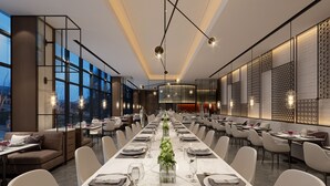 Un comedor amplio con una larga mesa dispuesta para una comida, rodeado de asientos cómodos y grandes ventanales con vistas.