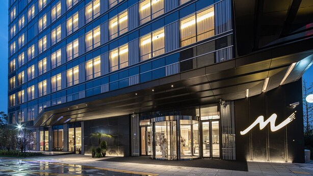 Un hotel moderno con fachada de vidrio, varios pisos y puerta giratoria.