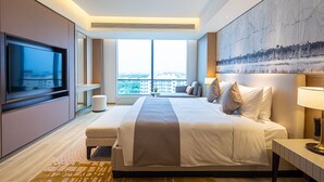 Una habitación de hotel moderna con una cama grande, un televisor de pantalla plana, un ventanal con vistas a la ciudad y un cuadro en la pared.