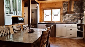 A wooden interior with a dining table, chairs, a kitchen area with a stove, and a stone wall.