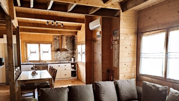 A wooden cabin interior with a dining area, kitchen, and a sofa.