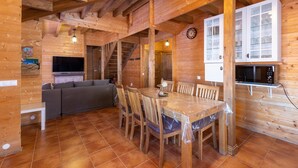 A wooden interior with a dining table, chairs, a sofa, a kitchen area, and a staircase.