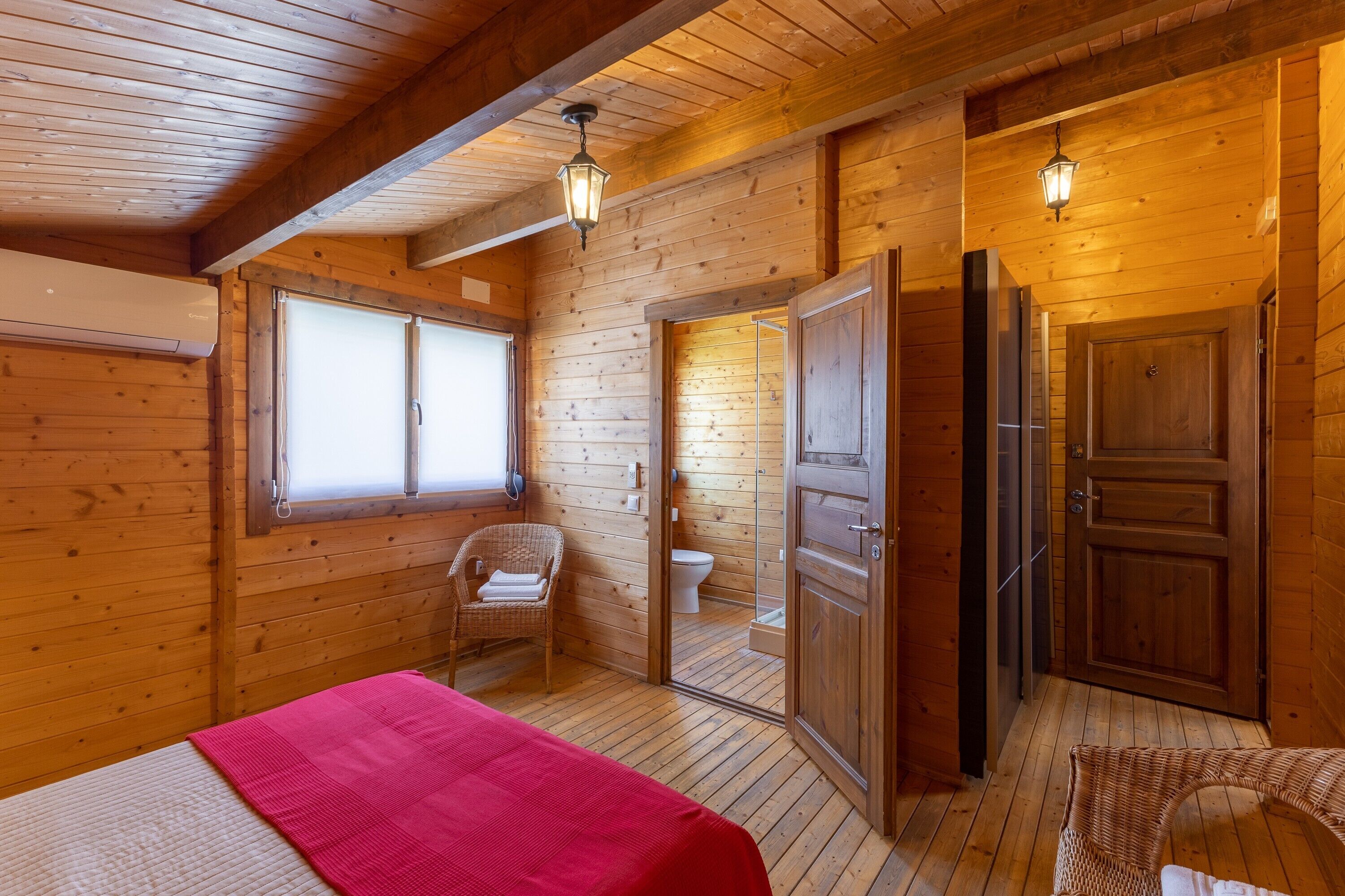 Ein Zimmer in einer Holzhütte mit einem Bett, einem Korbsessel, einer Holztür und einem Fenster.