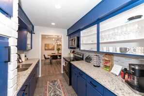 A modern kitchen with blue cabinets, a granite countertop, and a built-in microwave. There is a dining area visible in the background.