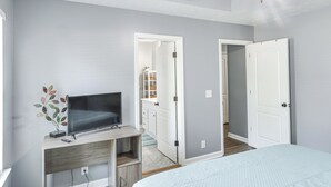 A bedroom with a bed, a TV on a wooden stand, and a door leading to a bathroom.