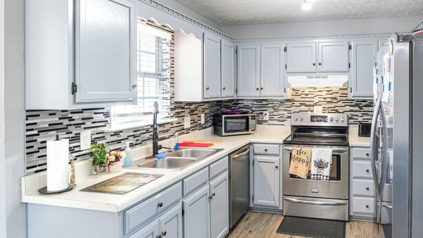 A modern kitchen with light gray cabinets, a stainless steel refrigerator, a microwave, and an oven.
