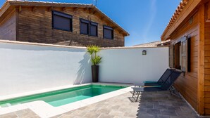 Una piscina con muelle de madera, una planta en maceta y un edificio con tejado de baldosas.
