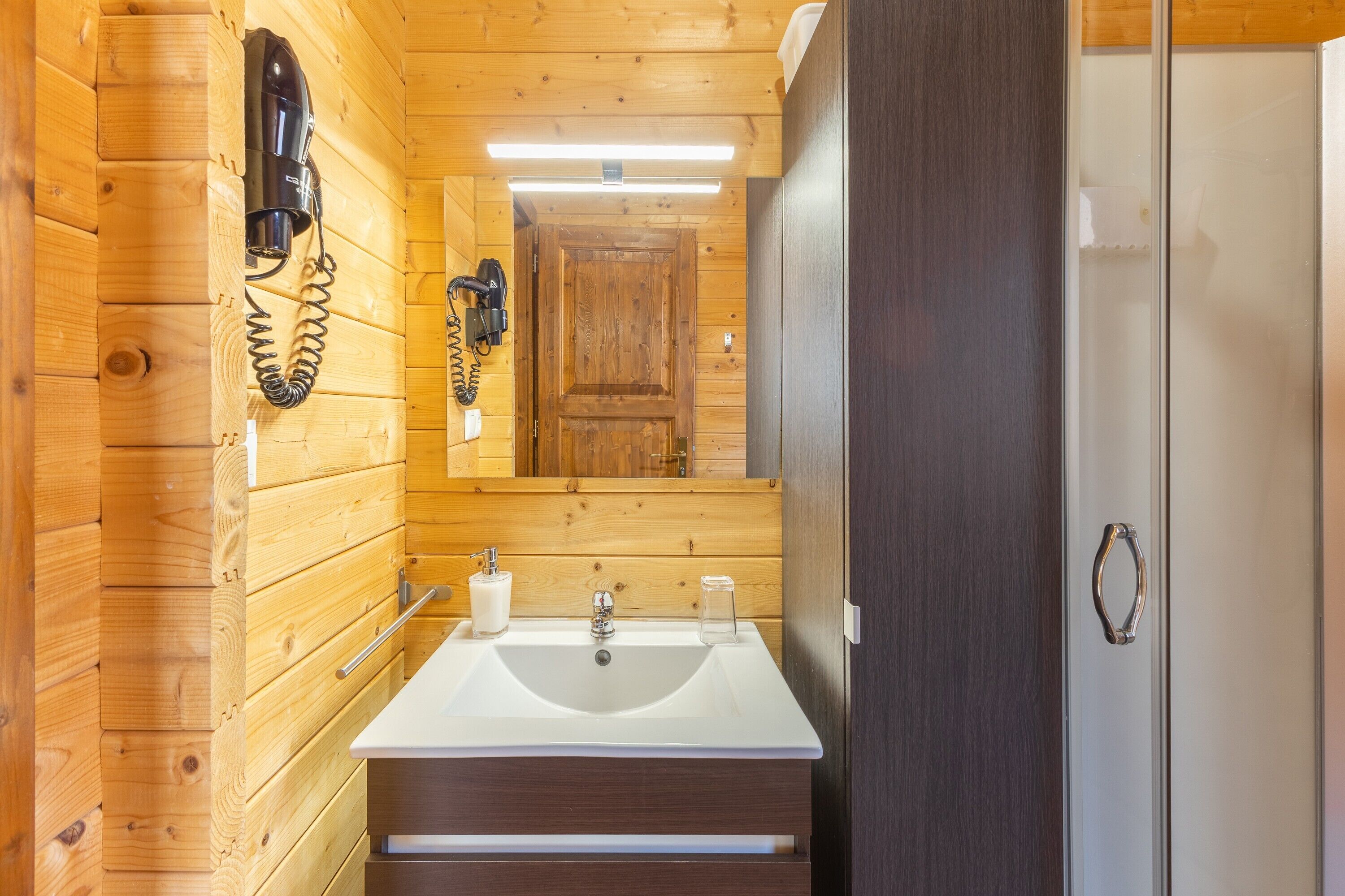 A wooden cabin bathroom with a sink, mirror, and a hairdryer mounted on the wall.