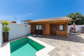 A wooden cabin with a swimming pool, a patio with chairs, and a table. - Casa Rural 'La Dehesilla' in Toledo – Cozy Retreat for 4 with Private Plot (Cobisa)