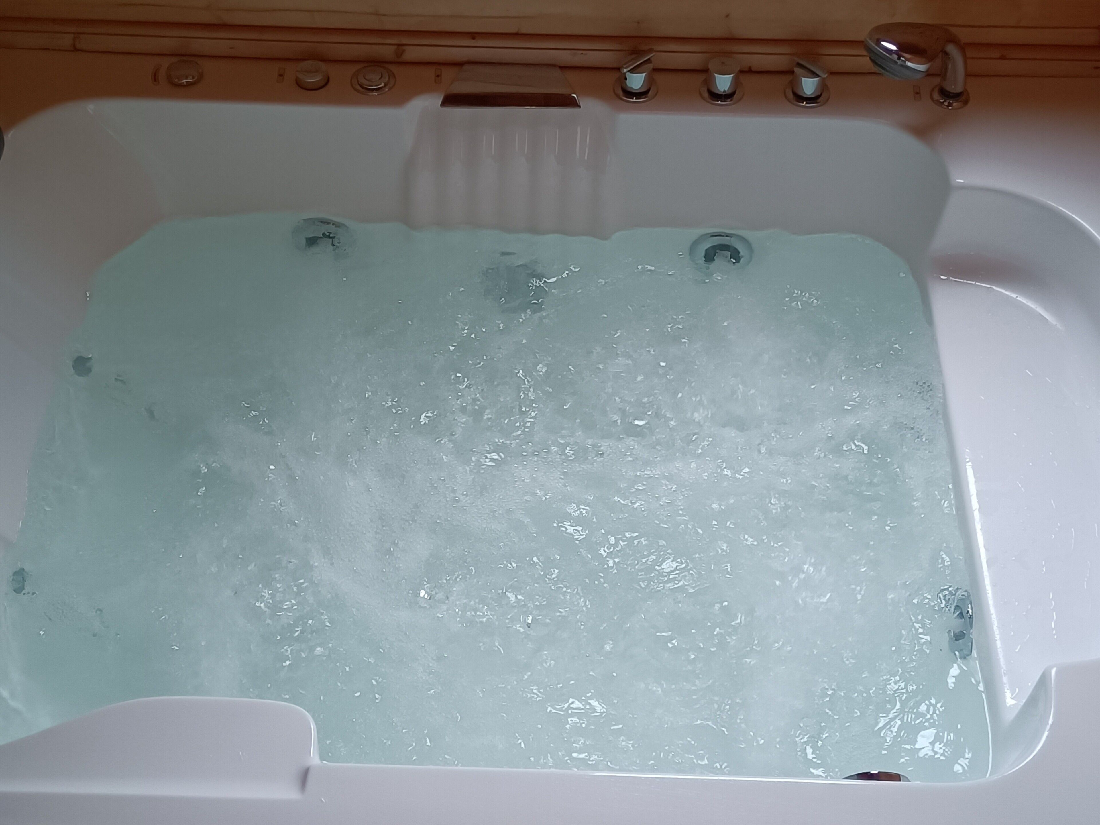 A bathtub filled with water, a wooden panel wall, and a faucet.