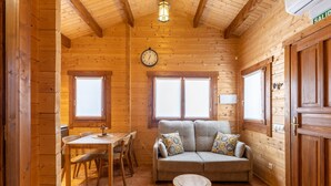 Interior de una cabaña de madera con sofá, mesa de comedor, sillas, un reloj y una puerta con un letrero.