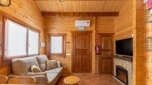 Interior de una cabaña de troncos con un sofá, una pequeña mesa redonda, una chimenea y un televisor.