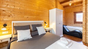 Un dormitorio de cabaña de madera con cama, lámparas de noche, armario y bañera.