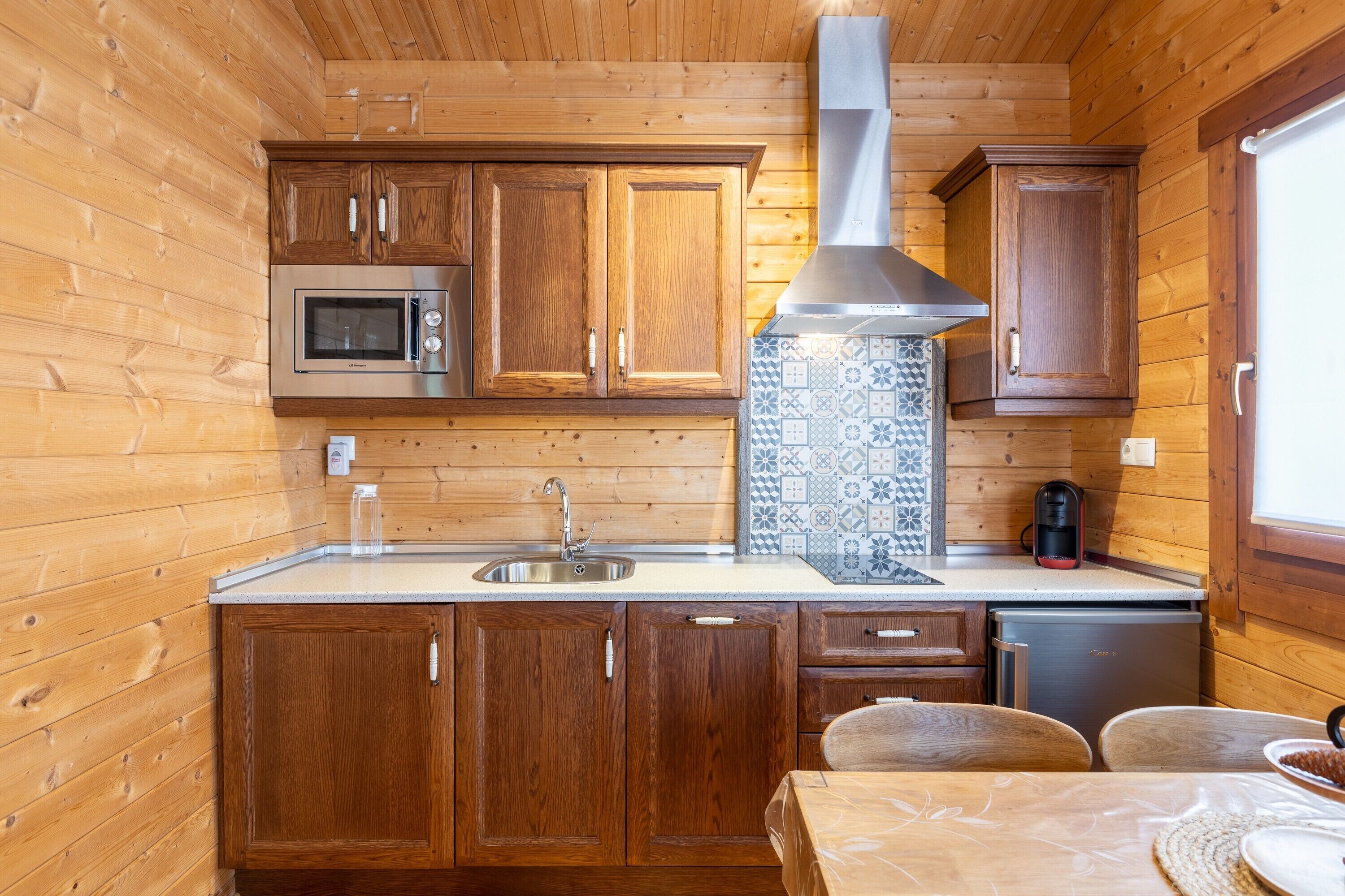 Cocina compacta con armarios de madera, un microondas de acero inoxidable, un fregadero y una cafetera.
