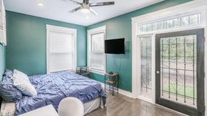 A bedroom with teal walls, a bed with blue bedding, a ceiling fan, a TV mounted on the wall, and a sliding glass door leading to an outdoor area. -  LakeHouse with rooftop and views of lake. (Chicago)