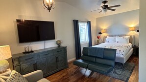 Un dormitorio moderno con una cama, ventilador de techo, televisor y sofá.