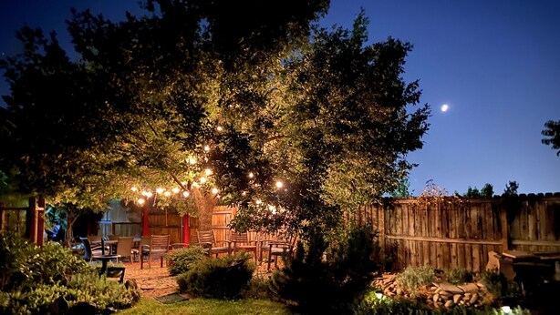 Un patio al aire libre con luces colgantes, mobiliario de madera y un cerco de madera.