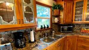 Una cocina con armarios de madera, encimera de piedra, lavavajillas, cafetera y microondas.