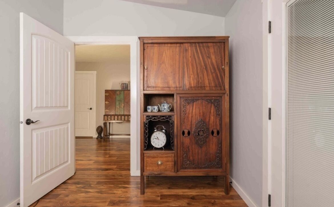 A hallway with a wooden cabinet, a white door, and a closed shutter.