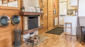 A cozy room with a fireplace, wooden walls, a kitchen area, and a dining table. - Saariseläntie 8 d7 by Interhome (Inari)
