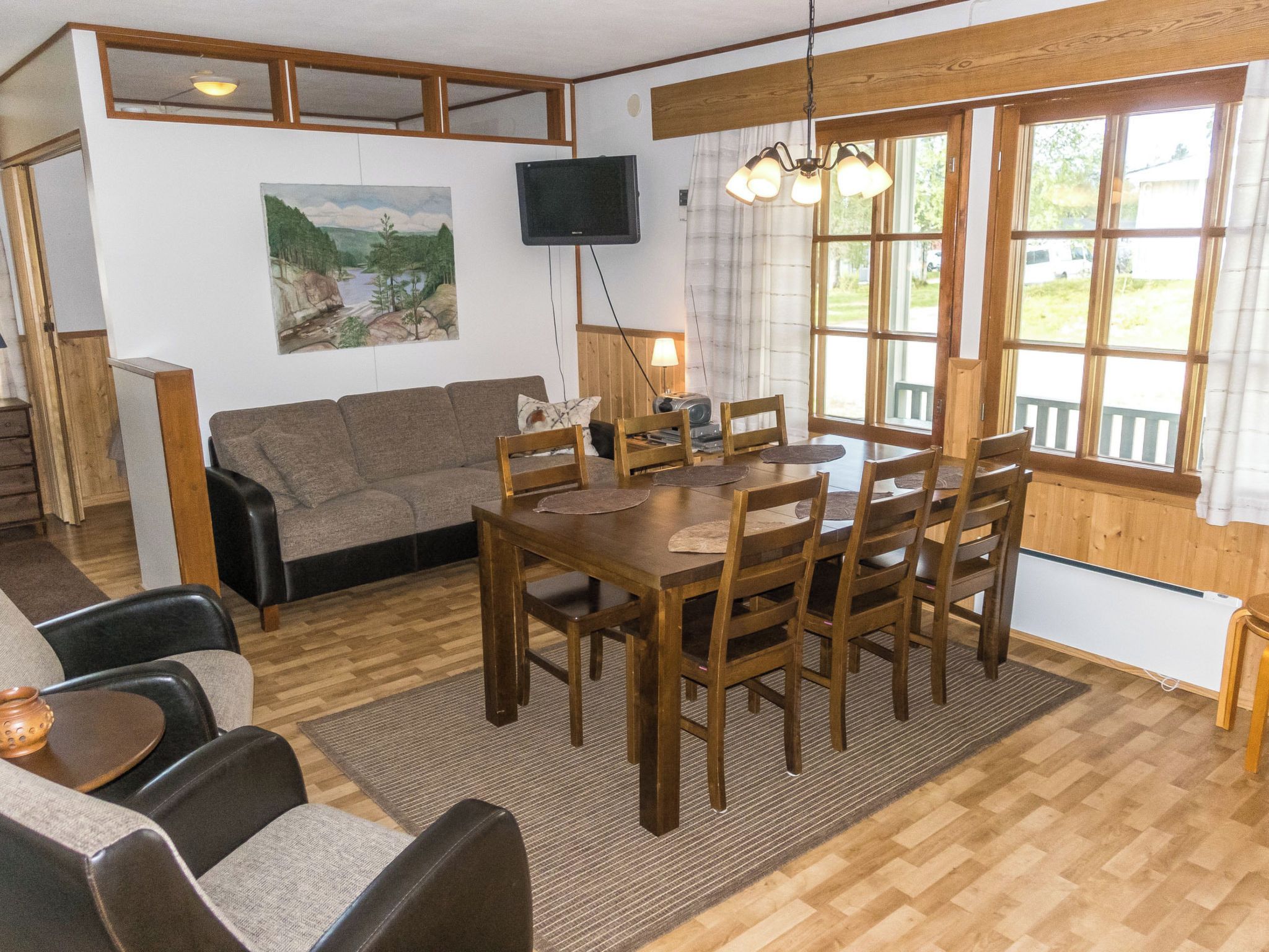 Un salon chaleureux avec une table à manger en bois, des chaises, un canapé et un téléviseur fixé au mur.