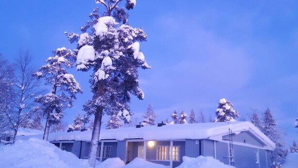 A snow-covered house with a visible door and windows, surrounded by snow-laden trees. - Saariseläntie 8 d7 by Interhome (Inari)