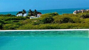 A swimming pool with clear turquoise water, surrounded by lush greenery and a view of the ocean.