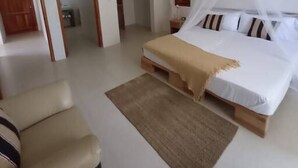 A bedroom with a bed, a ceiling fan, a wooden floor, and a door.