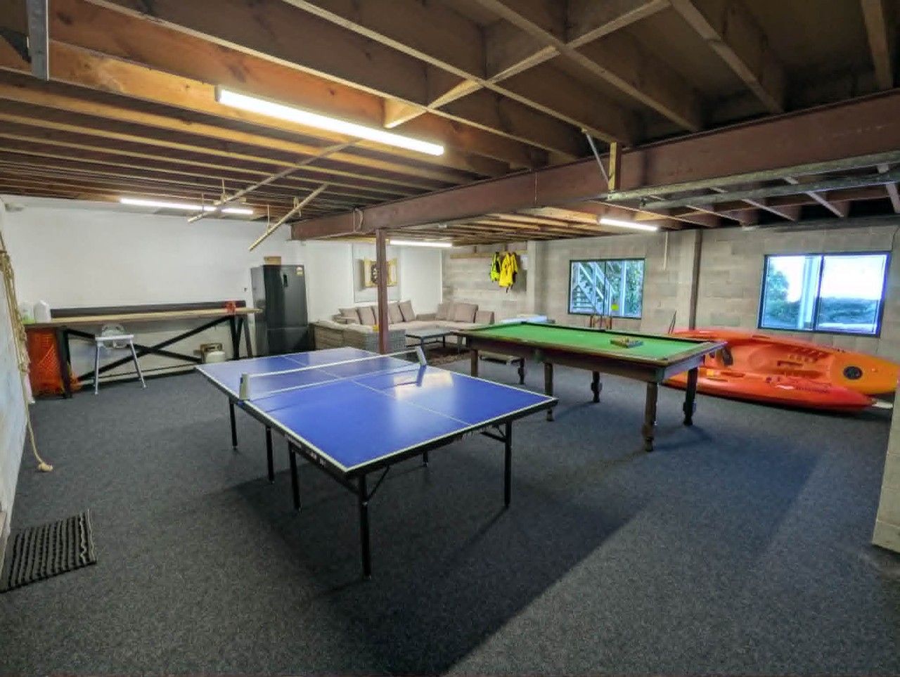 Una habitación con mesa de ping pong, mesa de billar y mesa de billar con fieltro verde. Hay una ventana con vistas al exterior.