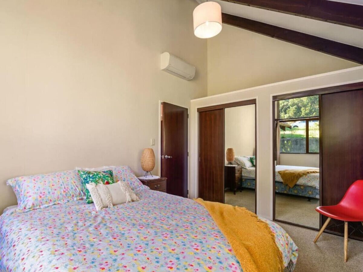 Un dormitorio con una cama, una silla roja, un espejo y un puerta corredera que da a un balcón.
