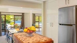 A modern kitchen with a stainless steel refrigerator, a wooden island with a fruit bowl, and a dining area with a view. - Peaceful Lake Rotoiti Escape | Jetty, Kayaks & Clear Water Views (Rotorua)