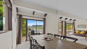 A dining area with a table, chairs, and a view of the outdoors. - Peaceful Lake Rotoiti Escape | Jetty, Kayaks & Clear Water Views (Rotorua)