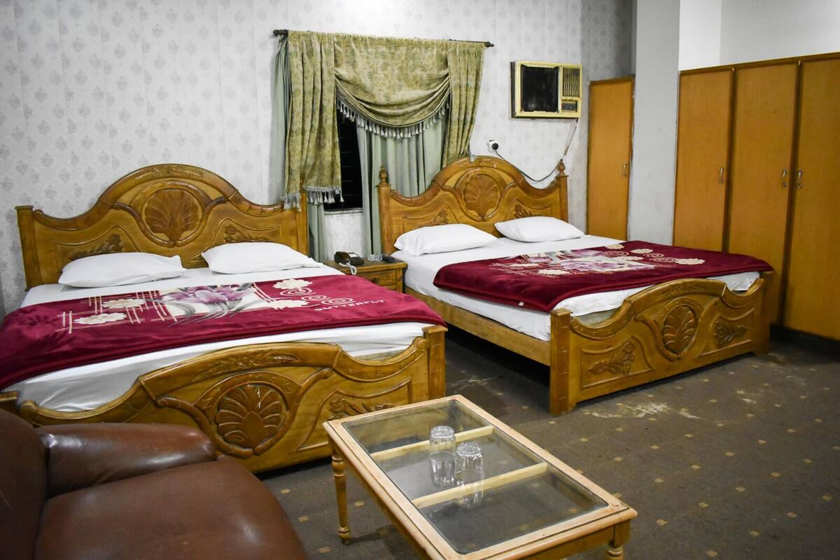 A room with two wooden beds, a glass-top table with two glasses, a brown leather chair, and a wardrobe.