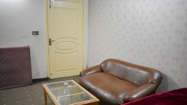 A room with a brown leather sofa, a glass-top coffee table, a patterned red sofa, and a plain yellow door. - New Capital Hotel (Lahore)