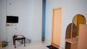 Een kamer met een aan de muur bevestigde televisie, een klein tafeltje met een dienblad, een paar schoenen op een mat en een houten deur.