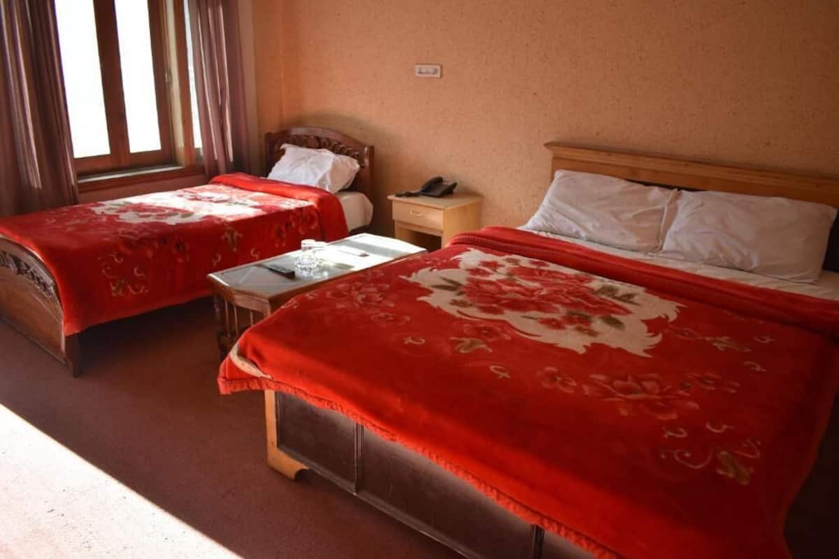 A room with two beds, each with a red floral bedspread and white pillows. There is a small table in the center with a glass of water and a book.